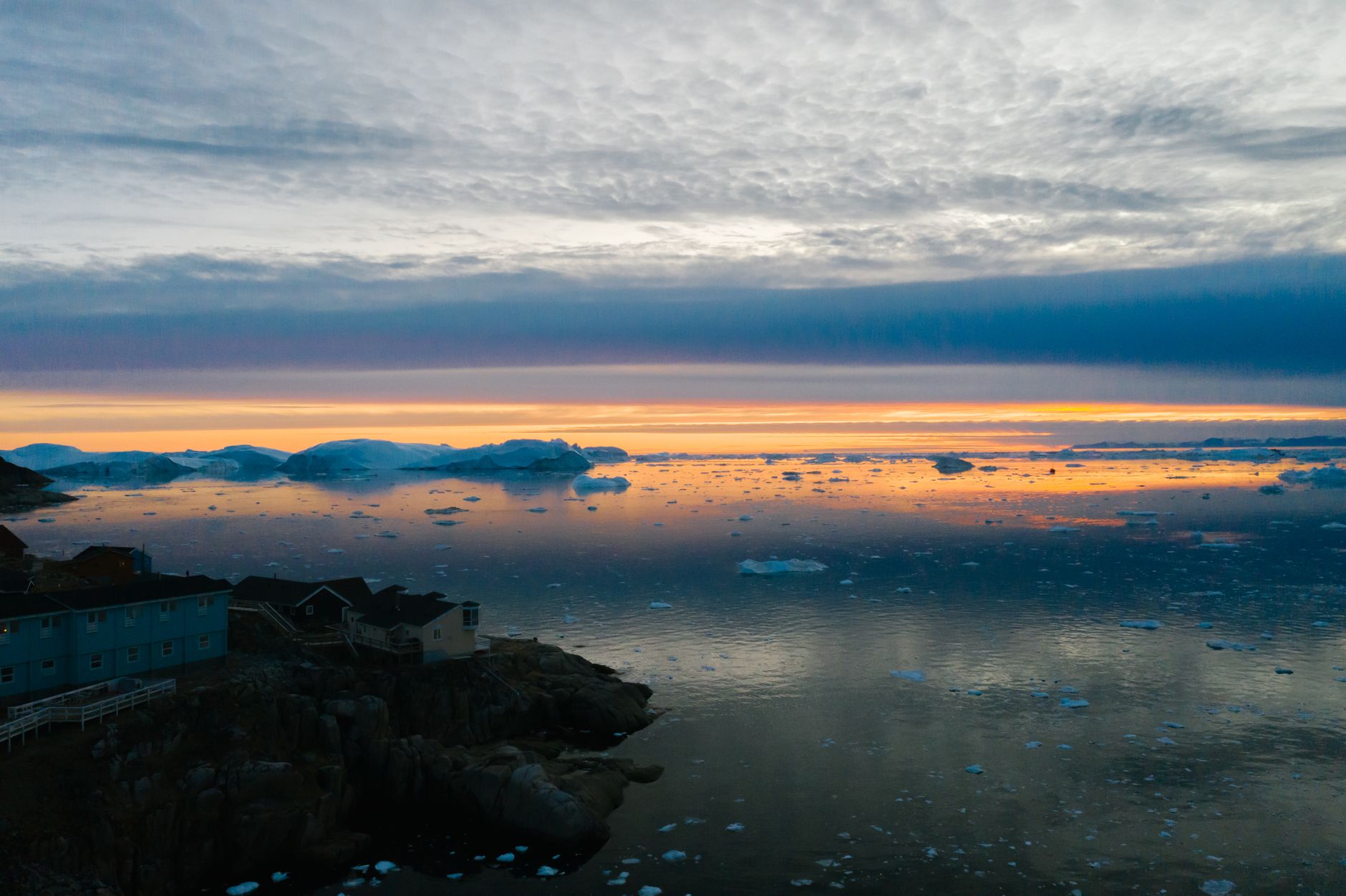 Breathtaking sunset over a coastal village with floating icebergs and calm sea reflections.
