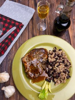Delicious pork chop with black beans and rice served on a wooden table.