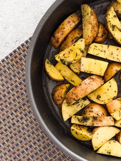 Free Top view of herb-seasoned sliced potato wedges in a baking pan, ready for roasting. Stock Photo