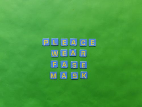 Free Text displaying 'Please Wear Fase Mask' on a vibrant green surface using colorful tiles. Stock Photo
