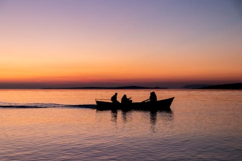 Silhouettes of People Sailing in Boat on Sunset