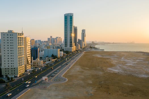 Aerial view of a coastal city with skyscrapers, streets, and sea at sunset, showcasing urban life.