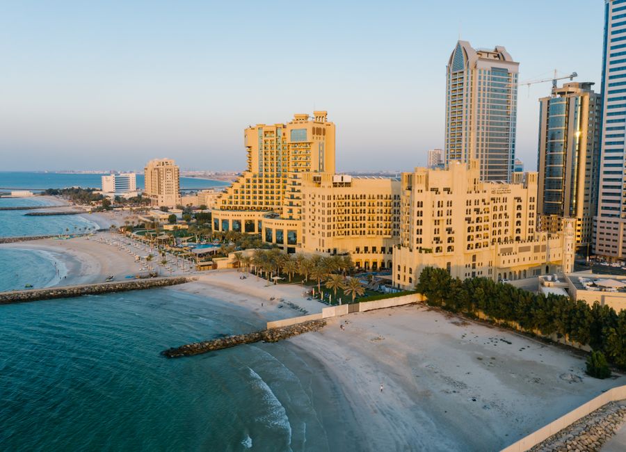 A stunning aerial view of Ajman's coastline with towering hotels and the tranquil beach at sunset.