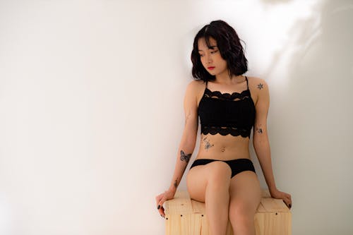 A Tattooed Woman in Black Crop Top Sitting on a Wooden Surface