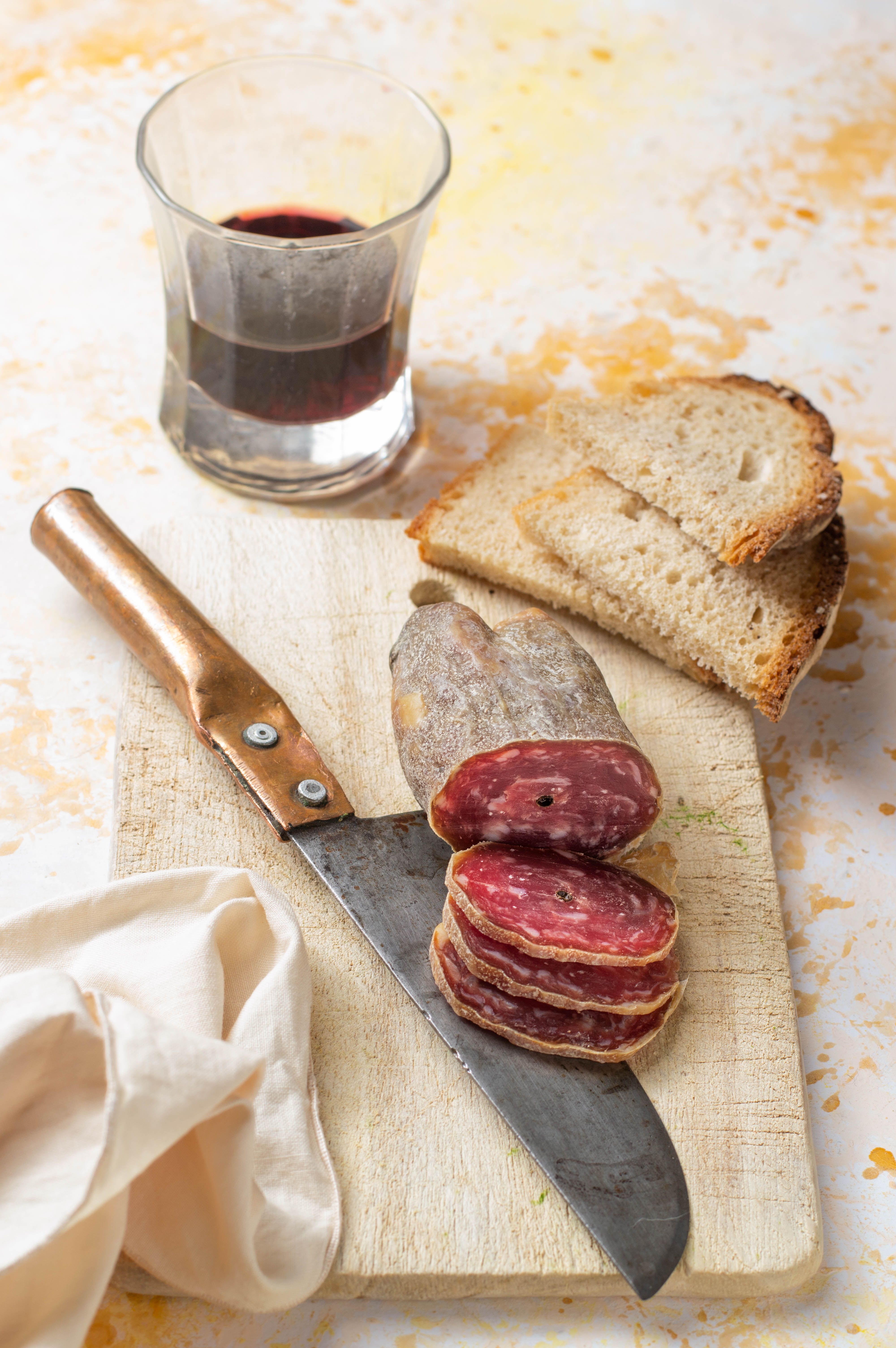 A rustic setup featuring sliced salami on a board with bread and red wine.