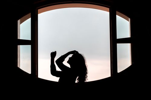 Free Dramatic silhouette of a woman posing by an arched window at sunset. Stock Photo