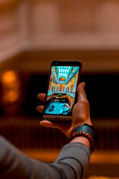A person holds a smartphone showing a colorful architectural interior with a blurred background.