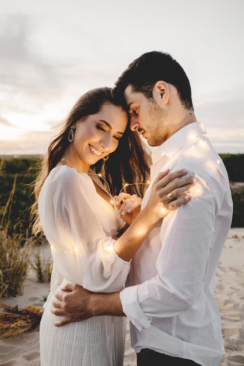 Side view of romantic soulmates embracing gently while standing with illuminating garland on sand