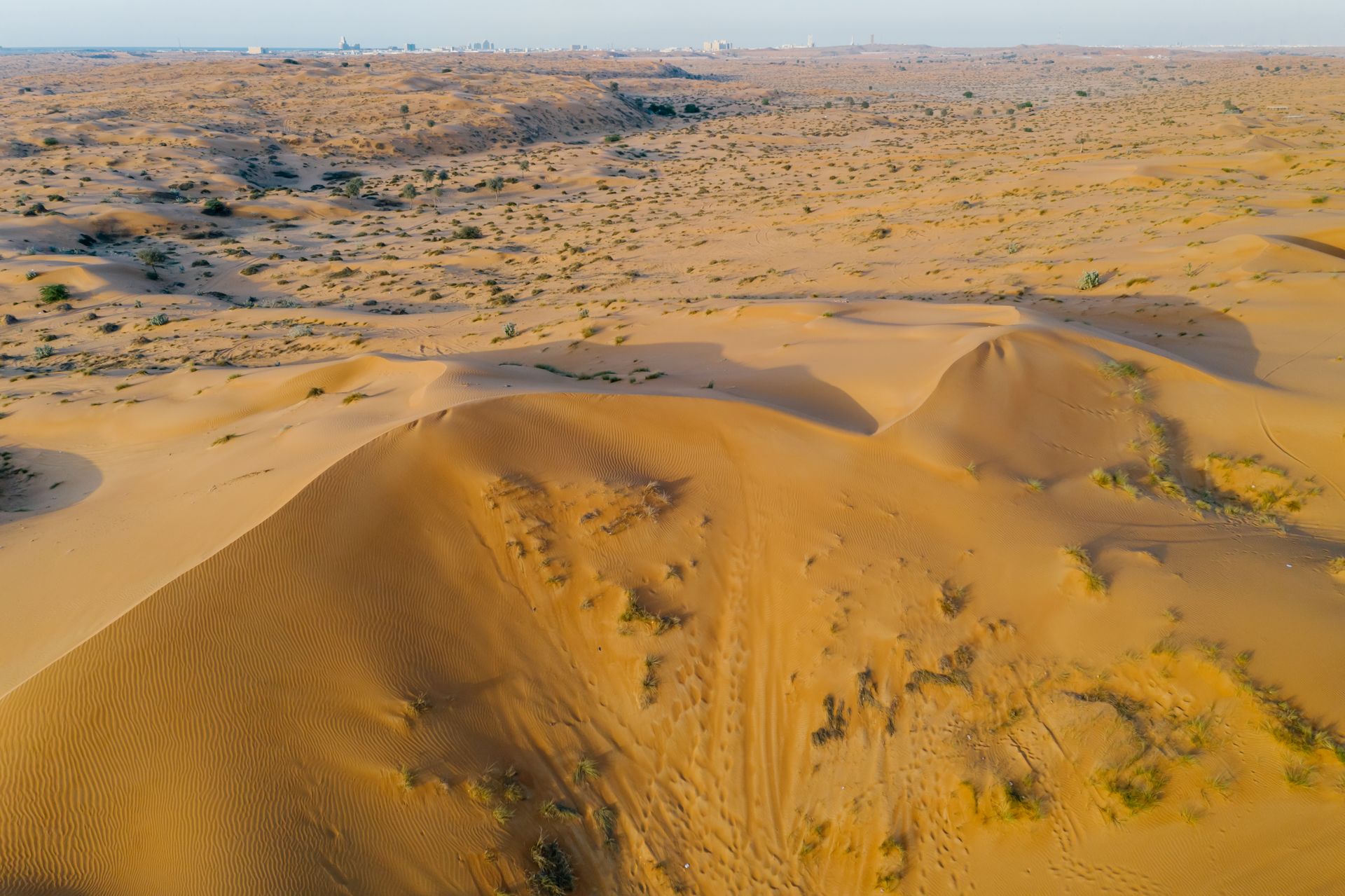 Drone shot capturing the vast and sandy landscape of desert dunes under a clear sky.
