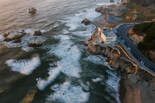 A stunning aerial view capturing ocean waves crashing against a coastal building at dusk.