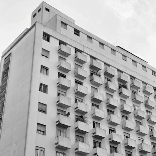 Black and white of multistory house facade with windows and balconies in cloudy day
