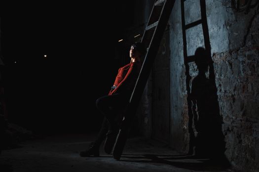 A woman poses dramatically on a wooden ladder in an abandoned building with moody shadows.