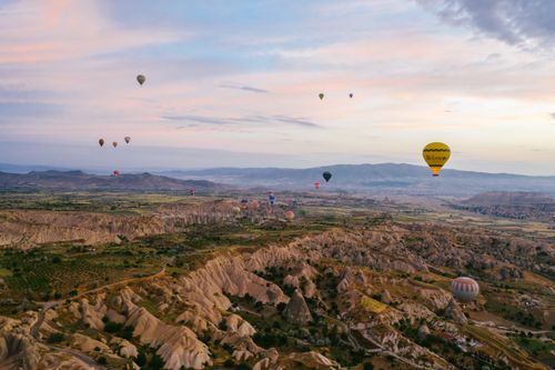 Free A serene view of hot air balloons floating over the rocky landscape of Cappadocia at sunrise. Stock Photo