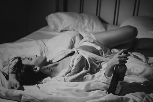 Free A grayscale image of a woman with wine on a bed, evoking a moody atmosphere. Stock Photo