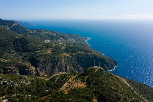 Free Breathtaking aerial view of lush forest along a rugged coastline with clear blue sea. Stock Photo