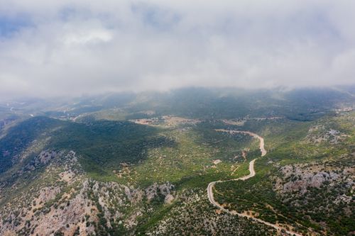 Free A breathtaking aerial view showcasing a winding road through a lush, fog-covered mountain landscape. Stock Photo