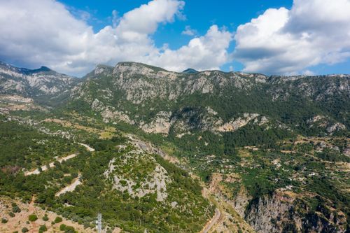 Free A breathtaking aerial view showcasing lush forests and rocky mountains under a bright blue sky. Stock Photo