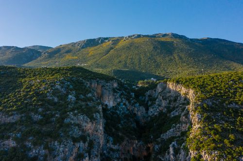 Free A breathtaking aerial shot of lush green mountains and cliffs under a clear blue sky. Stock Photo