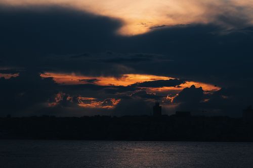Free Silhouetted skyline against a dramatic sunset sky over a calm water body, creating a moody atmosphere. Stock Photo