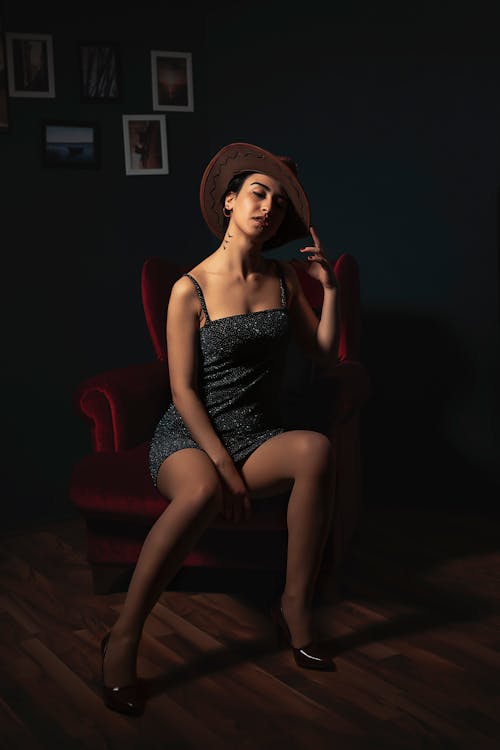 Woman in a Mini Dress and a Hat Sitting on a Velvet Armchair 