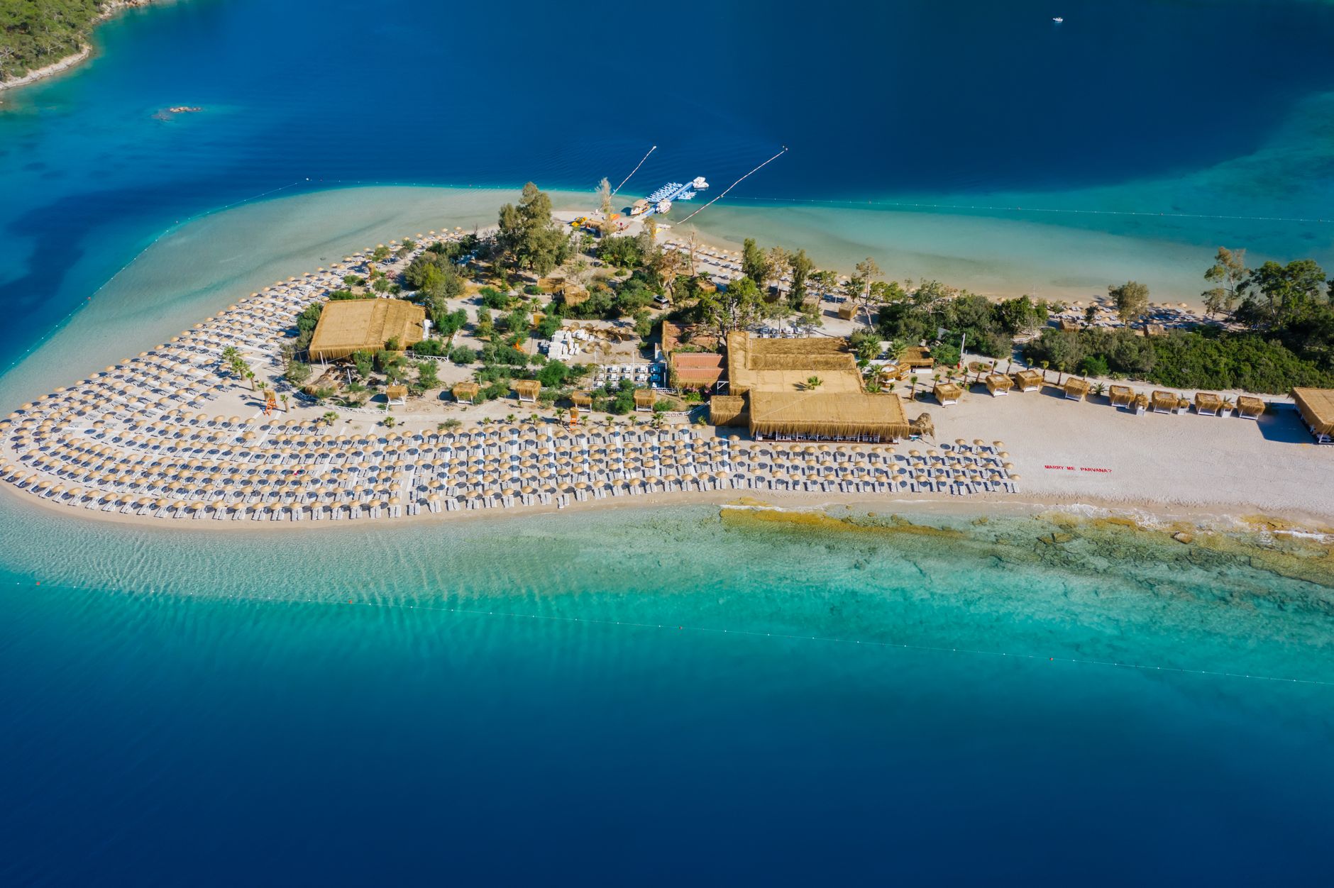 Stunning aerial view of a beach peninsula with sun loungers and clear turquoise waters.