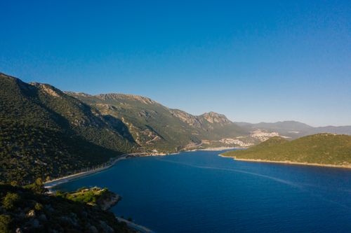 Free Stunning aerial view of a mountainous coastline with a clear blue sea under a bright sky. Stock Photo
