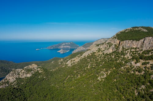 Aerial View of Green Mountain Beside Blue Sea Under Blue Sky