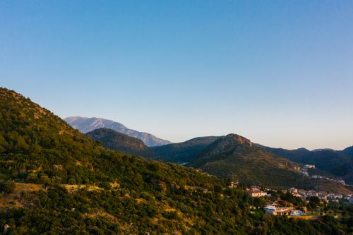 Free Aerial view of lush green mountains and a small town under a clear blue sky. Stock Photo