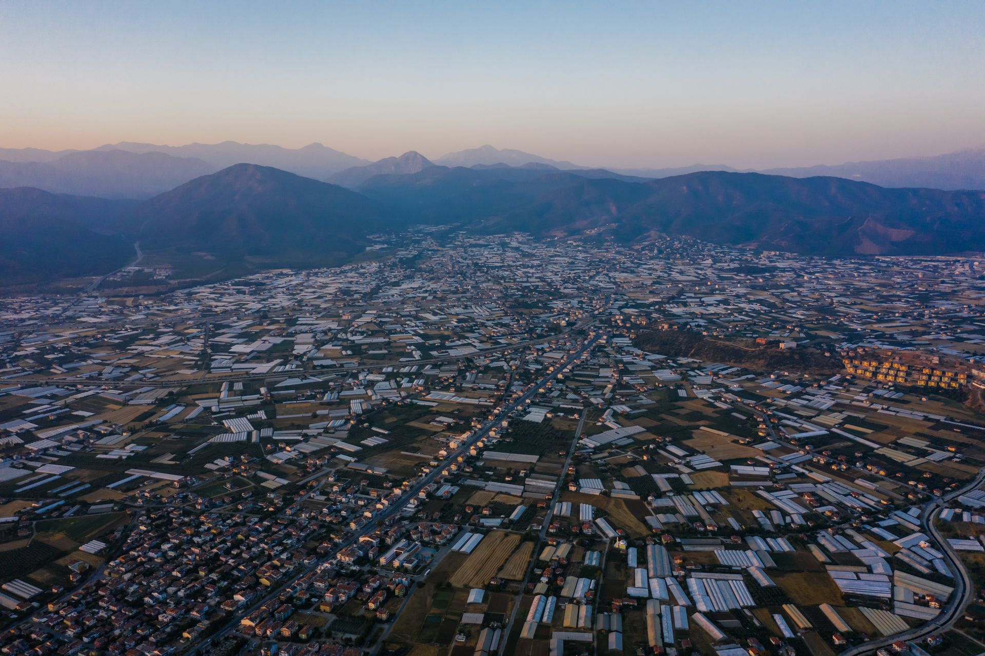 Aerial photograph showcasing a sprawling urban landscape with mountains in the background during dusk.