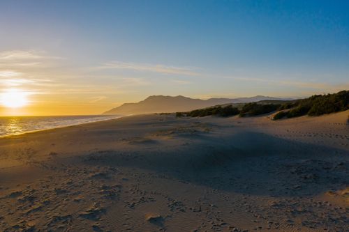 Free A breathtaking sunset over a serene beach with mountains in the background, ideal for travel and nature lovers. Stock Photo