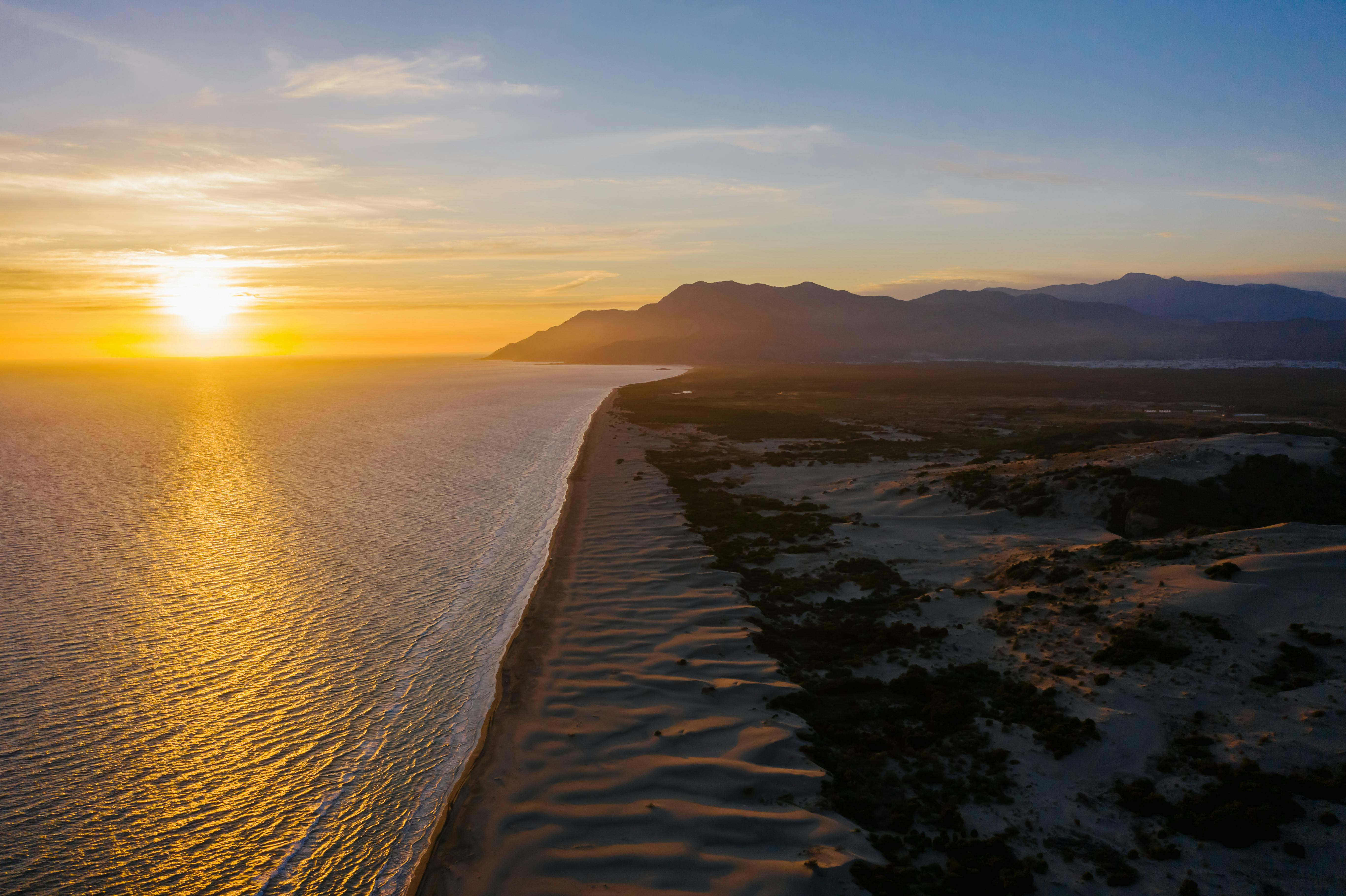 Patara Beach Turkey with endless golden sand dunes, turquoise Mediterranean waters, and ancient Lycian ruins visible in distant hills under soft morning light