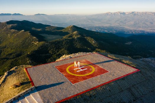Aerial view of a helipad with people on a scenic mountain peak during the day.