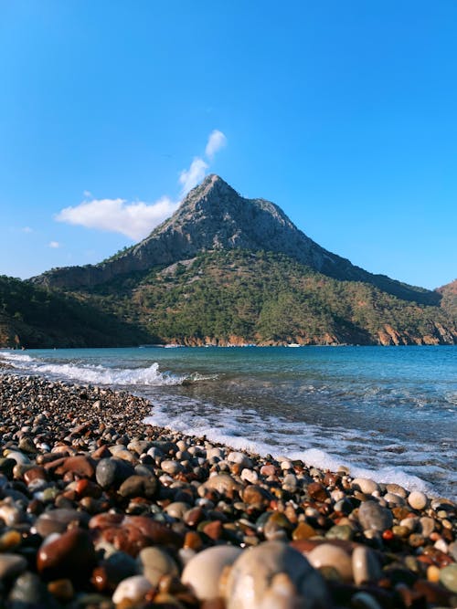 Free A Rocky Shore With Mountain in Distance Under the Blue Sky Stock Photo