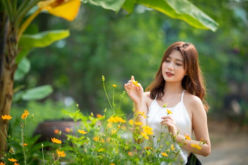 A Woman in White Tank Top Touching a Yellow Flowers