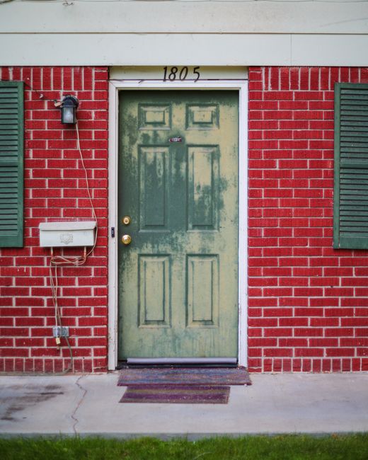 A rustic green door set against a vibrant red brick wall with green shutters.
