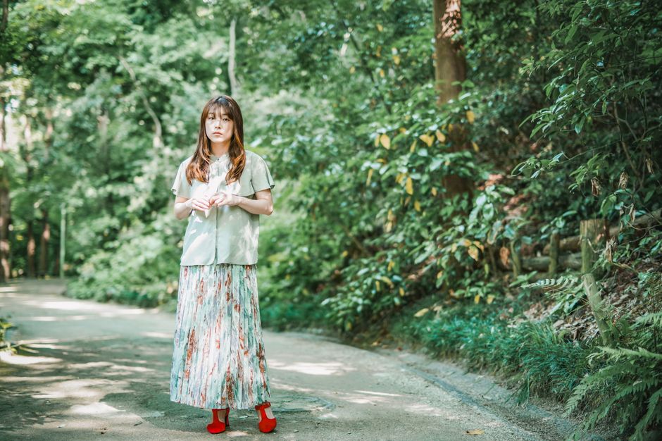 豊かな緑に囲まれた森の小道を歩く女性。