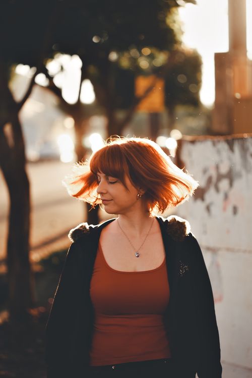 Free Portrait of a redhead woman posing outdoors with bokeh lights during sunset. Stock Photo
