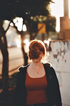 A redhead woman walks outdoors at sunset, captured in a soft bokeh effect.