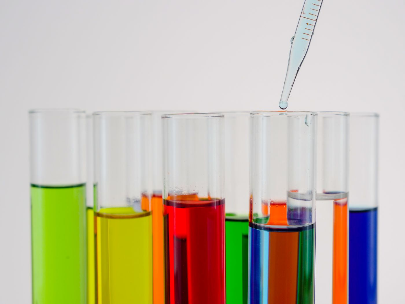 Rows of laboratory test tubes with colorful liquid ingredients and a pipette