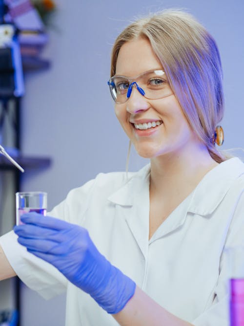 Woman in White Coat Smiling while Doing an Experiment