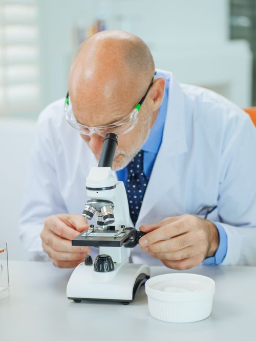 Free A researcher wearing safety glasses closely examines samples under a microscope. Stock Photo