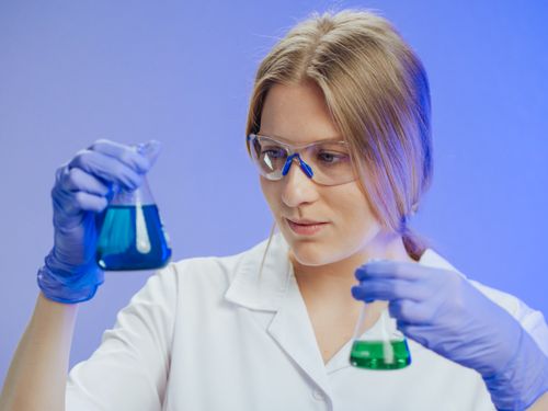 Free Woman scientist holding Erlenmeyer flasks with colored liquids in a laboratory. Stock Photo