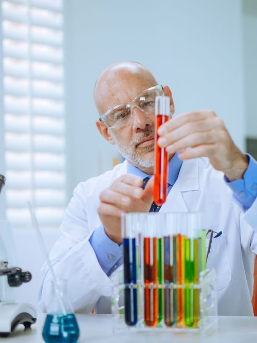 Free Scientist in a lab coat analyzing colorful chemical liquids in test tubes, focusing on research and discovery. Stock Photo