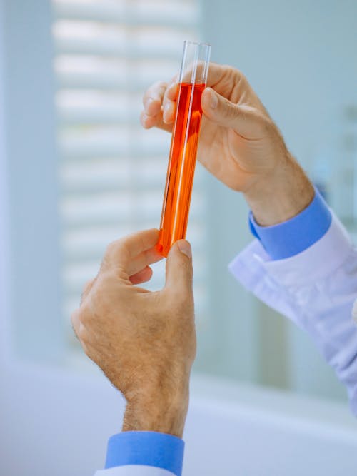 Free Close-Up View of a Person Holding a Test Tube with Orange Liquid Stock Photo