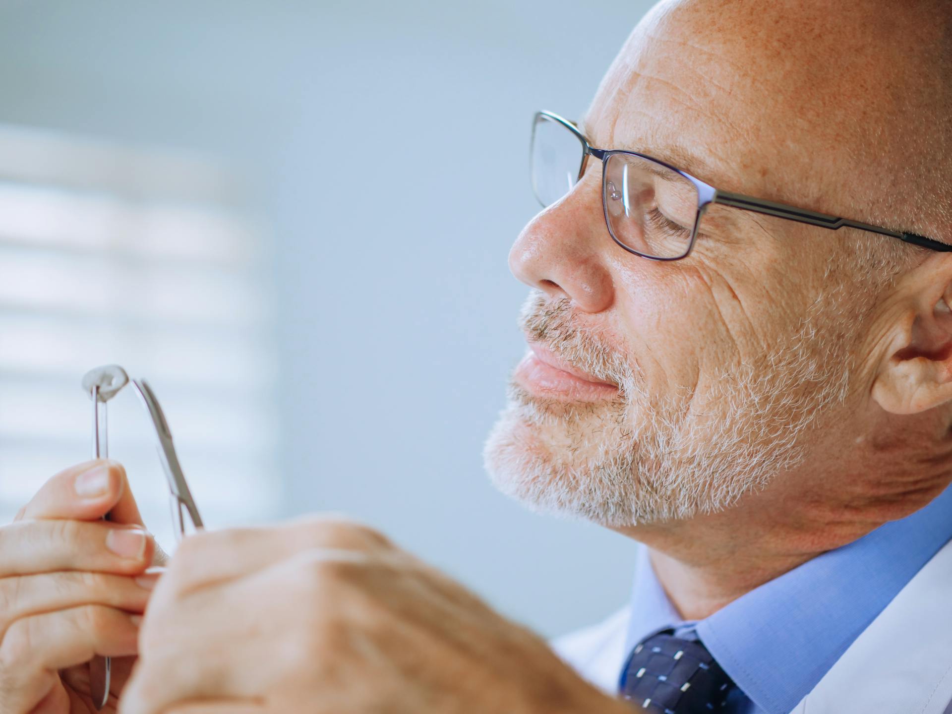 Elderly male scientist focused on laboratory work with glasses in hand.