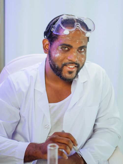 Free Scientist in a lab, wearing goggles and a white coat, smiling confidently. Stock Photo