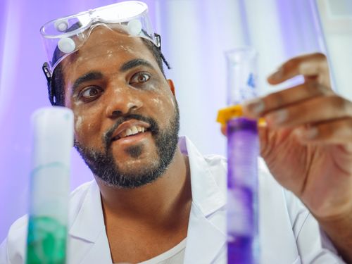 Free Scientist in a lab coat examining colorful liquids in test tubes, focused and intrigued. Stock Photo