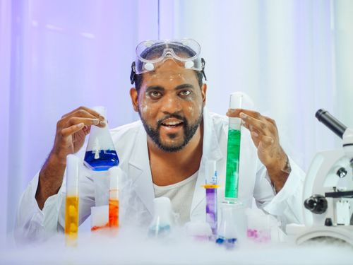 Free A scientist in a lab coat performs colorful chemical experiments with various lab equipment. Stock Photo