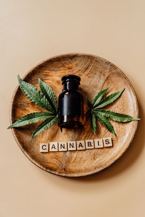 Free A bottle of cannabis surrounded by leaves on a wooden plate with scrabble tiles. Stock Photo