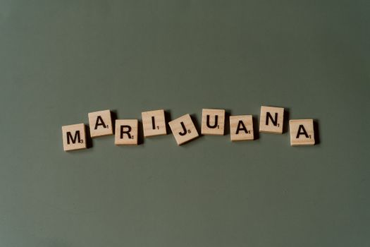 Scrabble tiles arranged to spell 'Marijuana' against a green backdrop in a minimalist style.